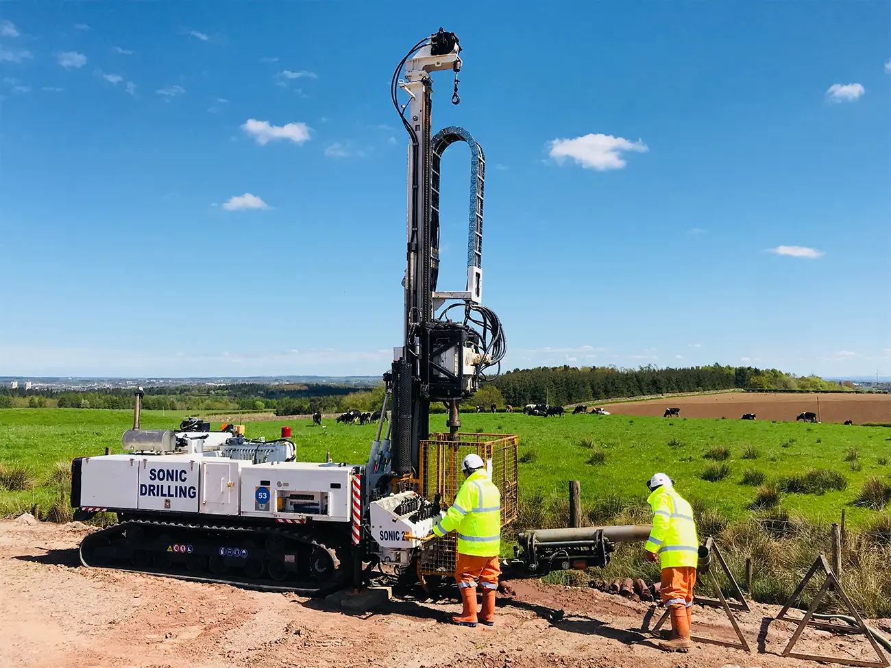 Sonic drilling rig, with two workers in PPE.