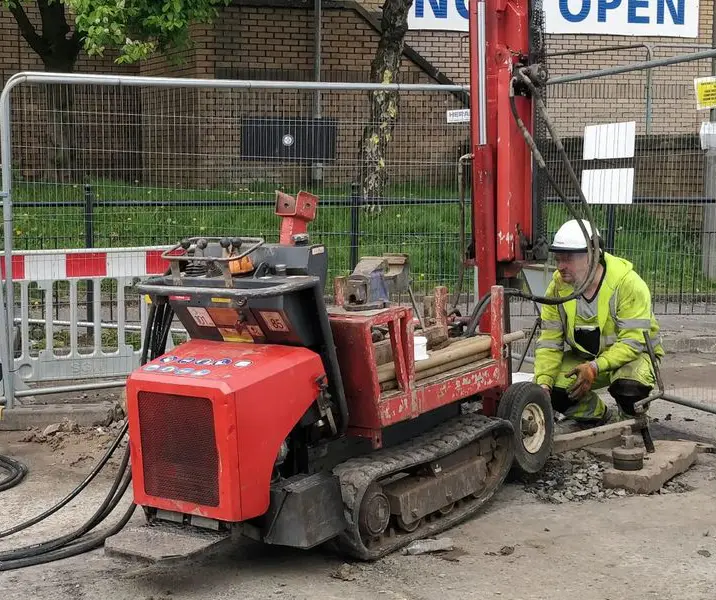 man in PPE using drill to collect soil samples from the ground